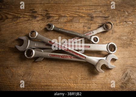 Various chrome vanadium wrenches, some with visible brand names, lie scattered on a rustic wooden background, suitable for repair and DIY themes. Stock Photo