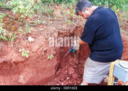 Individual works diligently in rich red soil, using jackhammer tool to break up ground Stock Photo