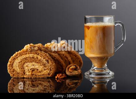 Walnut and buttercream roll: a traditional Oriental pastry. Dessert with walnuts and coffee latte on a black reflective background. Cake with brown su Stock Photo