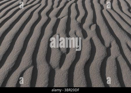 Close-up of wavy sand patterns created by the wind in a desert, forming natural abstract lines and textures. Stock Photo
