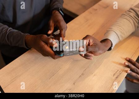 African American male clerk and customer exchanging payment on card reader at cafe service counter. Transaction, commerce, digital, technology, paymen Stock Photo