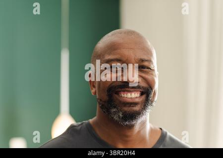 Middle-aged African American man smiling in living room with pendant lamp and green white panels. Portrait, celebration, cozy, contemporary, maturity, Stock Photo