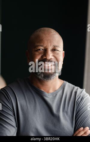 Senior African American man standing with arms crossed in studio near window wearing grey shirt. Portrait, confidence, minimalism, introspection, natu Stock Photo