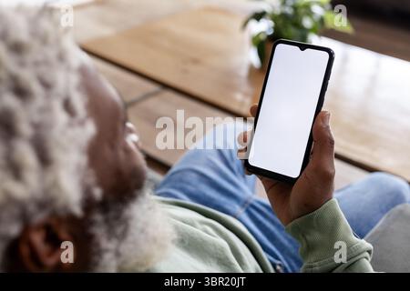 Senior African American man holding phone with blank screen at coffee table with plant, copy space. Retirement, relaxation, wellness, tranquility, lif Stock Photo