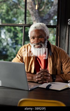 Senior African American man typing on silver laptop writing in notebook with pen at home office. Affection, professionalism, technology, lifestyle, co Stock Photo