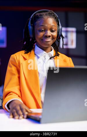 Woman wearing headphones at home using laptop to watch films on streaming services. Person using audio headset in living room, consuming entertainment with notebook on desk Stock Photo