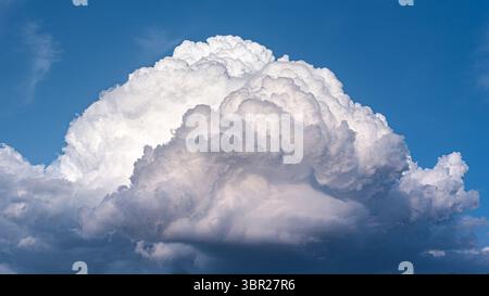 A towering cumulonimbus cloud forms in the sky during a summer thunderstorm, with a dark base and bright top, indicating intense weather activity. Stock Photo