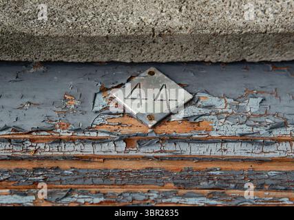 A metal diamond-shaped plate with the number 44 attached to an old wooden door with peeling paint Stock Photo
