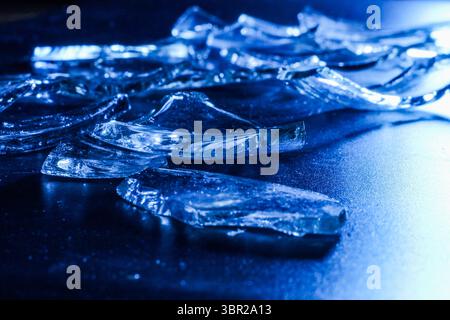 Broken Glass Shards on Dark Surface with Cold Blue Lighting Stock Photo