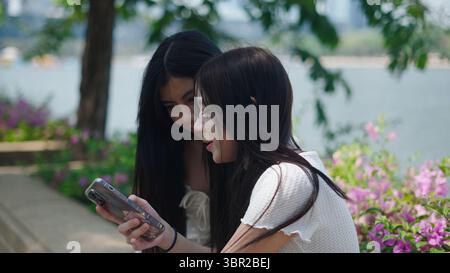 Two friends using a smartphone in a park, enjoying some time together outdoors Stock Photo