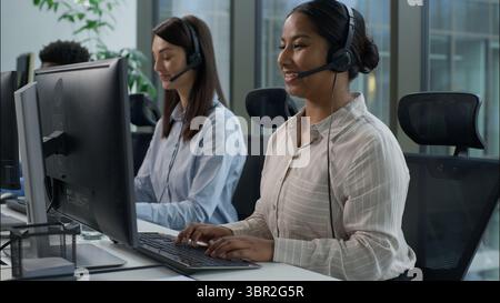Happy multiethnic business agents operators working call center computer helpline diverse Indian Caucasian businesswomen African businessman headset Stock Photo