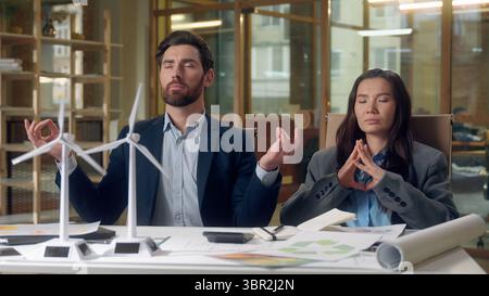 Multiethnic relaxed business team meditating wind turbine startup windmill models eco engineers Korean woman Caucasian man stress relief sustainable Stock Photo