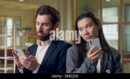 Multiethnic office workers Korean businesswoman Caucasian businessman using mobile phone business coworkers glancing colleagues screen curiosity Stock Photo