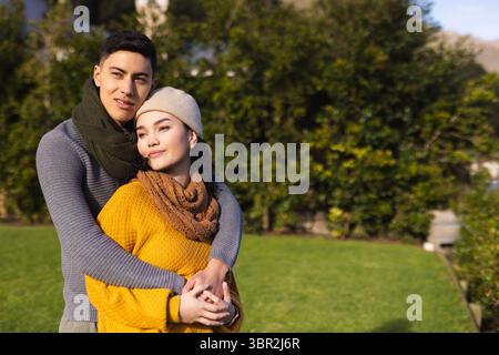 Asian couple embracing and standing on backyard lawn wearing knit scarves sweaters and beanie Stock Photo