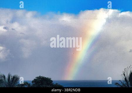 Rainbow steaking down from the clouds into the ocean. Stock Photo