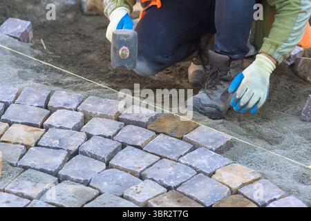 Laborer carefully positions cobblestones while maintaining alignment in construction setting during works day hours Stock Photo