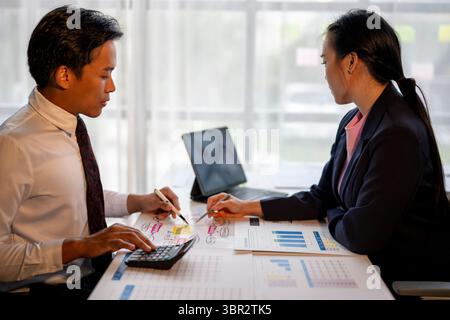 Two people are sitting at a table with papers and a calculator. They are discussing something important. The man is wearing a tie and the woman is wea Stock Photo