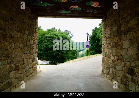 Gongju, South Korea - June 13th 2025: A shaded stone passage under the Gongsanseong Fortress gate opens onto a tree-lined path and hills, framed by so Stock Photo