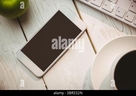 White smartphone is lying on wooden table in flat design with keyboard, coffee mug, green apple Stock Photo