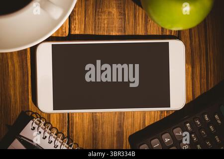 White-framed smartphone is lying on wooden desk with coffee cup, green apple, notebook, calculator Stock Photo