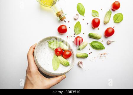 Fresh cut salad ingredients falling into white bowl on white minimal background. Ingredients for making dieting healthy vegetable salad Stock Photo