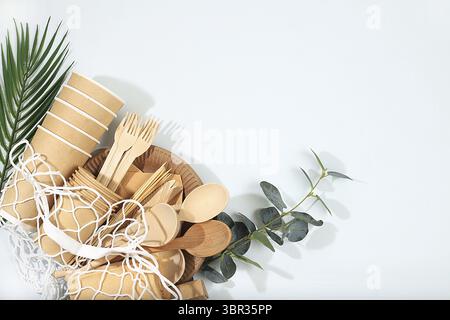 A set of environmentally friendly dishes in an eco bag on a sunny table. Paper cups, plates, kraft paper napkins, barbecue straws, wooden forks, spoon Stock Photo