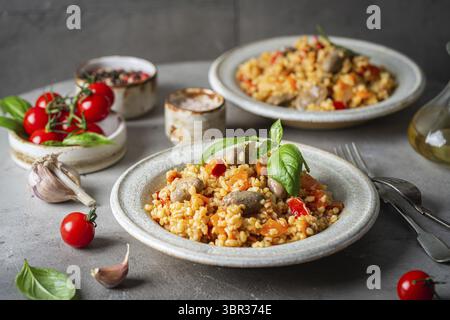 Bulgur with chicken hearts and vegetables. Delicious healthy dish on a gray background. Bulgur pilaf Stock Photo