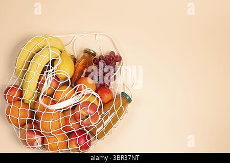 Lemons, oranges, tomatoes, apples, bananas, grapes and natural juice in a reusable bag, Fabric string bag with healthy vegan products for weight loss. Stock Photo