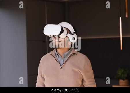 Senior Asian man wearing VR headset while standing under pendant light in modern lounge Stock Photo