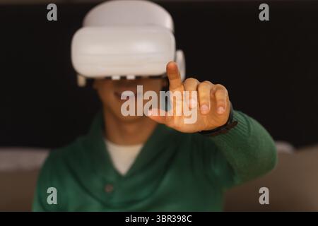 VR headset projecting holographic interface with hand reaching out on dark backdrop, copy space Stock Photo