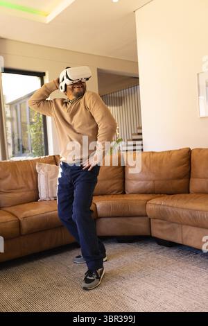 Senior Asian man standing in living room wearing VR headset near sofa and exploring virtual world Stock Photo