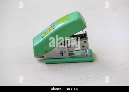 Close-up of a vintage mini stapler, silver staple pins visible inside. Resting on a light wooden desk, this classic office stationery item evokes nost Stock Photo