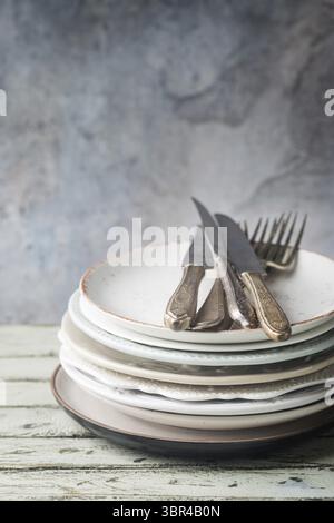 Stack of clean dinner plates with cutlery on top over wooden table. Pastel tones Stock Photo