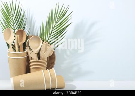 A set of environmentally friendly dishes on a sunny table. Paper cups, plates, kraft paper napkins, barbecue straws, wooden forks, spoons and knives, Stock Photo