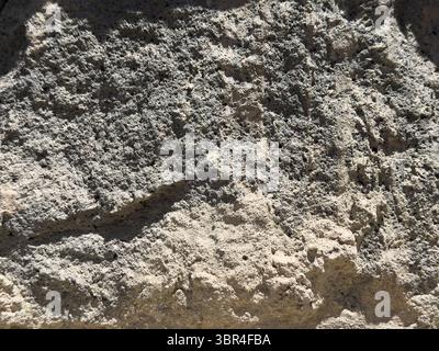 A wall made of stone. The wall is grey and has a few cracks. There are some small holes in the wall Stock Photo