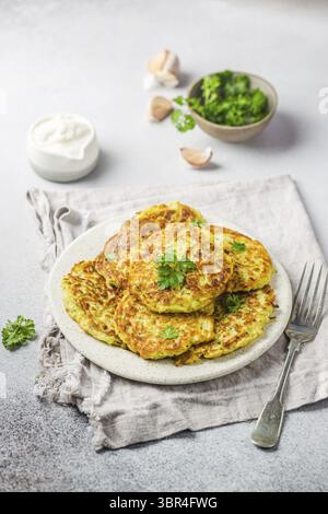 Green zucchini fritters, vegetarian zucchini pancakes with fresh herbs and garlic, served with cream sauce on white background, selective focus Stock Photo