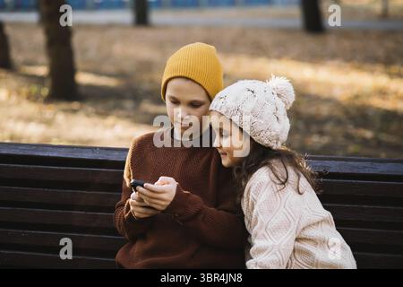 Kinder Maedchen und Jungen spielen Online-Spiele oder lesen soziale Netzwerke auf mobilen Smartphones. Kinder sitzen auf der Bank im Freien im Park Stock Photo
