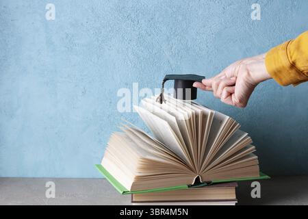 Woman's hand holding a paper student hat over an open book Stock Photo