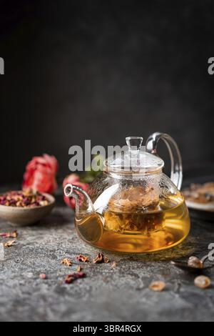 Herbal flower tea from the petals of rose in a glass teapot on dark gray background Stock Photo