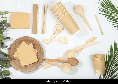 A set of environmentally friendly dishes on a sunny table. Paper cups, plates, kraft paper napkins, barbecue straws, wooden forks, spoons and knives, Stock Photo