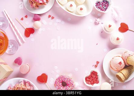 Romantic sweet dessert table for couple with pink waffles, donut, ice cream, macarons, heart shaped lollipops, candies. Valentine's day concept. Top v Stock Photo