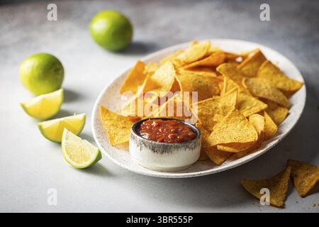 Single oval shaped white bowl of yellow corn tortilla nachos chips with salsa sauce over white table Stock Photo