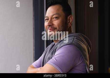 Asian man leaning near window against metal wall wearing purple shirt, grey sweatshirt, copy space Stock Photo