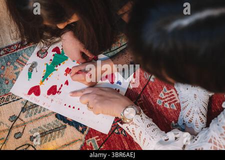 Children engaged in a creative drawing activity, crafting a colorful Christmas-themed artwork on paper with markers. The activity is set on a patterne Stock Photo