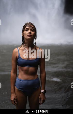 Young woman standing in front of a powerful jungle waterfall Stock Photo