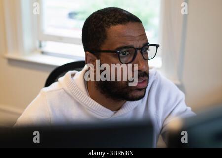 focused man with glasses works intently on a computer in an office Stock Photo
