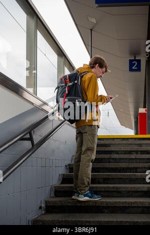 Man with backpack using smartphone at train station stairs Stock Photo