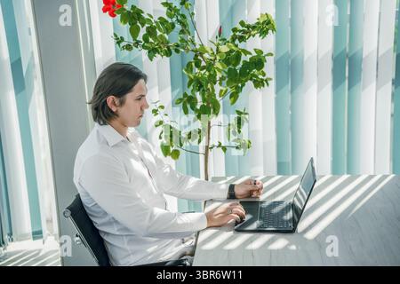 Man working on laptop in office, thoughtful pose. Modern interior. Stock Photo