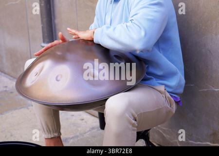 Close-up of a street musician’s hands performing rhythmic melodies on a handpan drum in an urban outdoor setting. Stock Photo