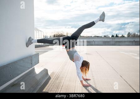 Woman Doing Handstand Against Wall Outdoors Stock Photo
